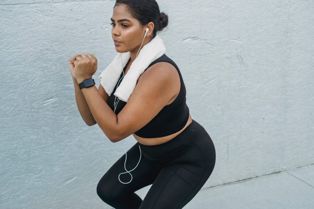 Fit woman exercising outdoors with headphones, towel, and fitness tracker, showcasing a healthy lifestyle.